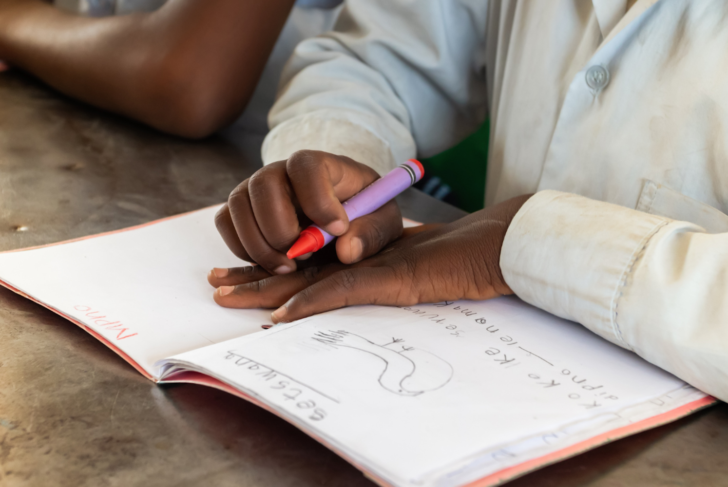 Student's hands holding crayon at school desk over notebook