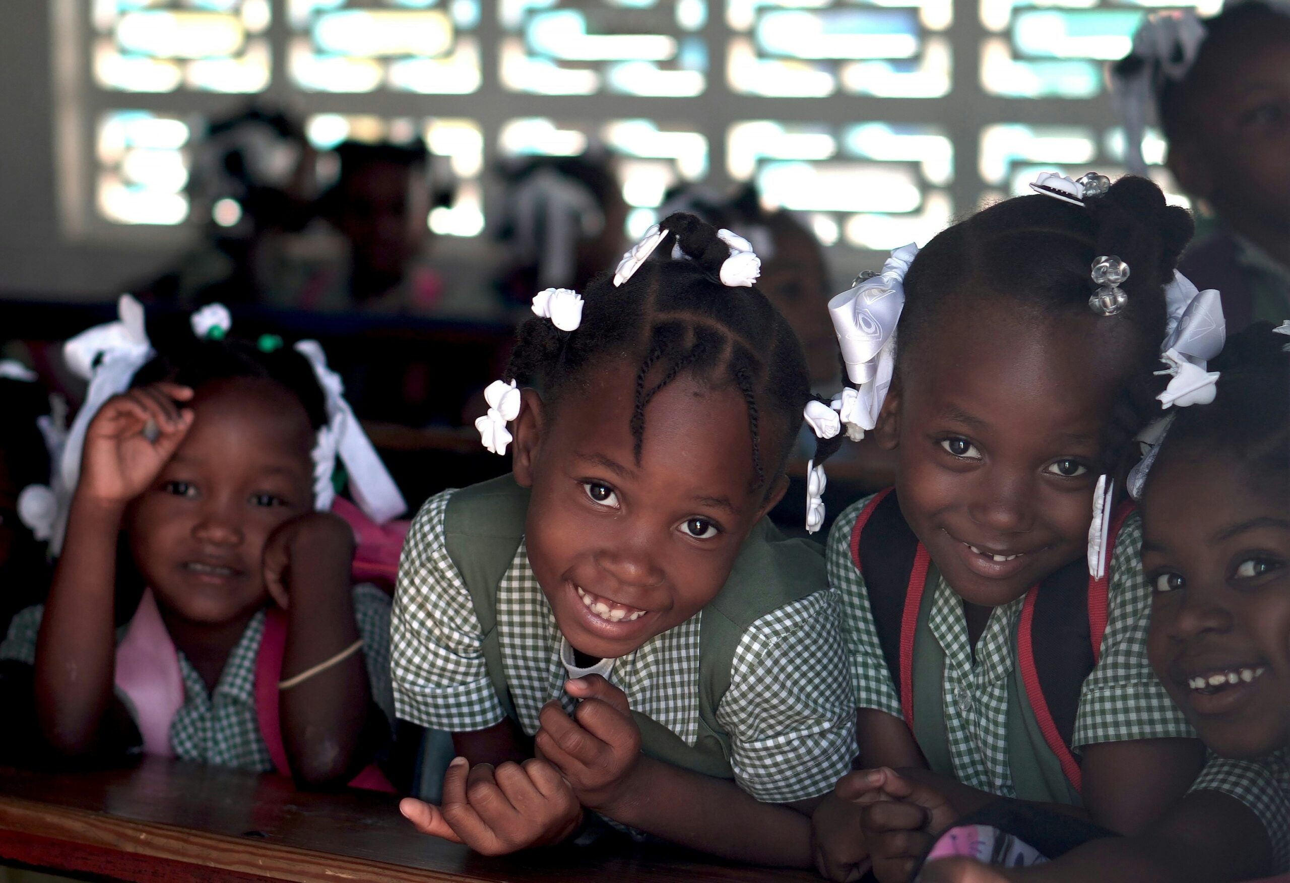 Girl students in uniforms in Haiti smiling and looking out of a window