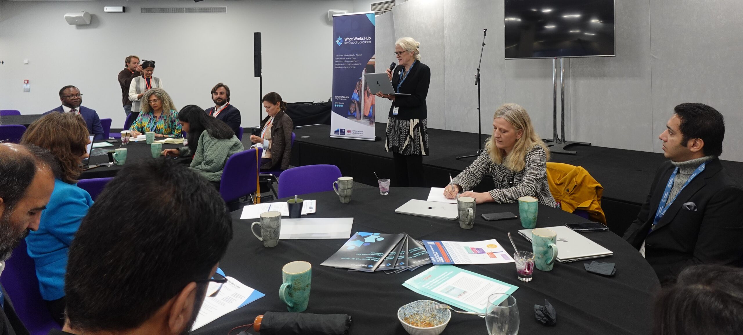 Participants attend an Education Labs session, with a facilitator speaking at the front while attendees discuss and take notes around round tables
